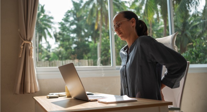 woman working at her desk looking in pain with hands on her lower back