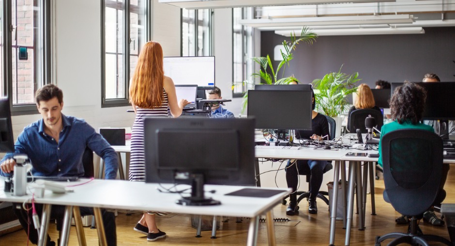 Employees in an open plan office setting working while making use of their office furniture.