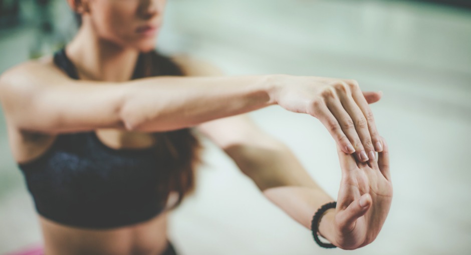 A young woman holding a stretch while stretching her hand and fingers doing muscle strengthening exercises to prevent RSI while doing yoga or pilates.