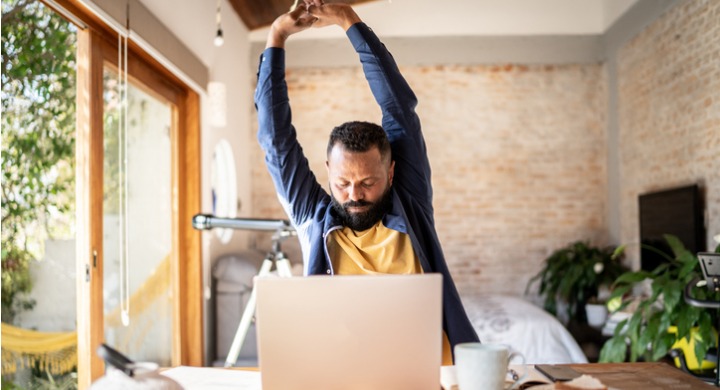 A man stretches as he works at home from his laptop with poor ergonomics.