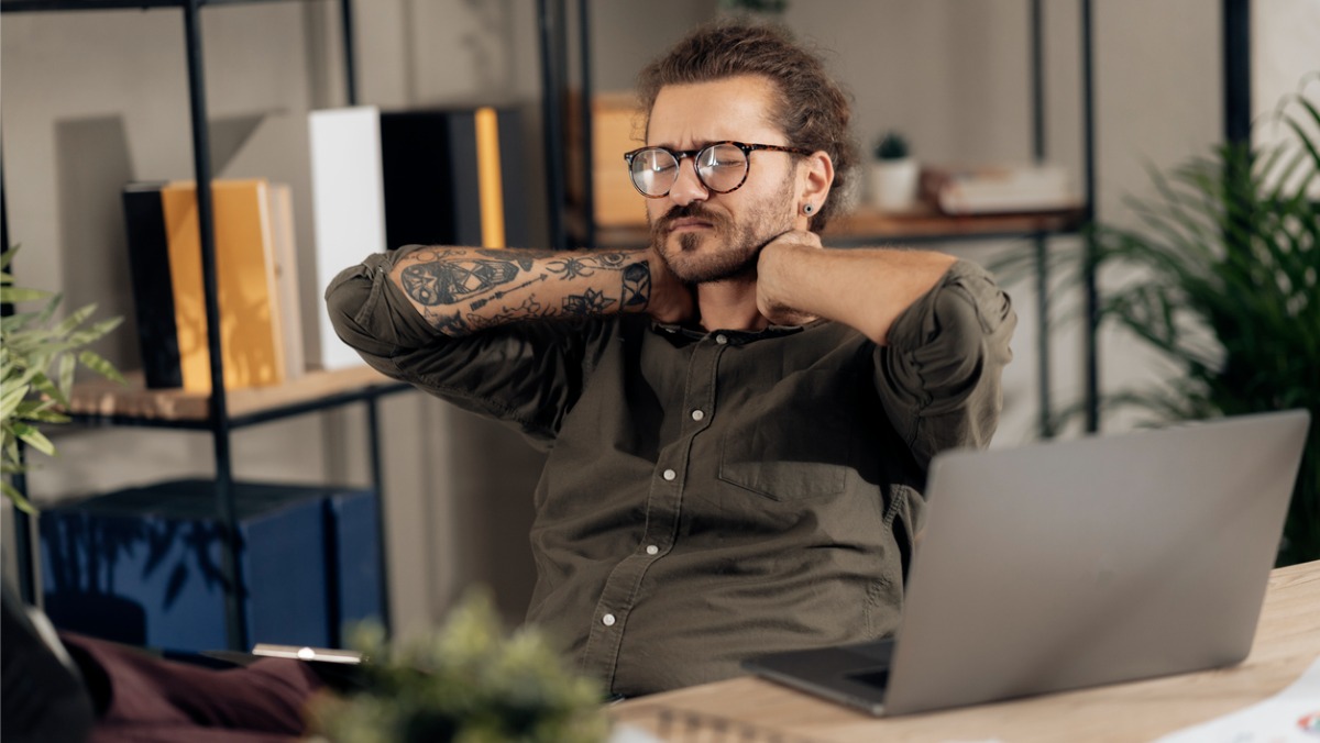 young man suffering from neck pain due to the lack of a laptop stand while working