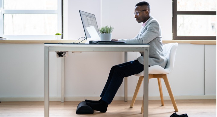 Man takes his shoes off to use an ergonomic footrest while at his workstation.