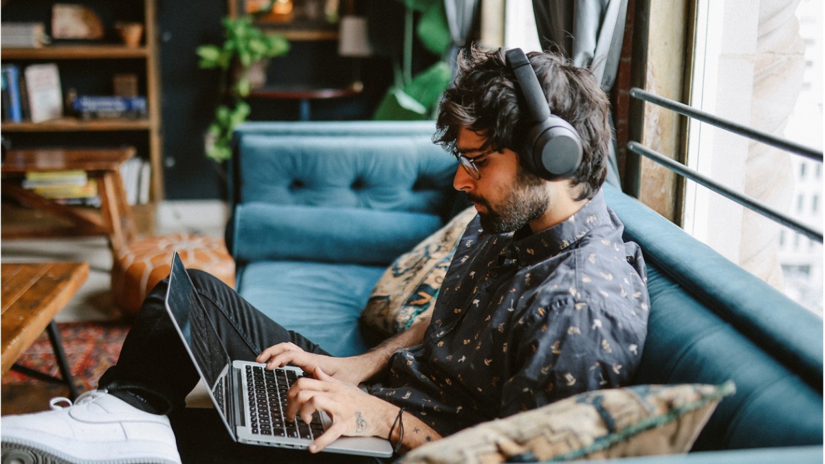 man sitting on a couch working from his laptop but not fulfilling his ergonomic requirements