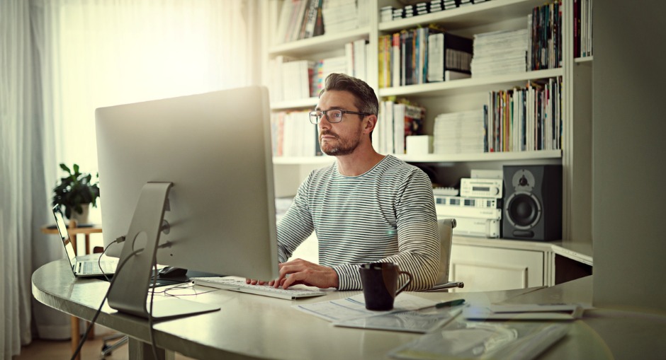 A caucasian middle aged man working in his ergonomic home office at the white sit stand desk.