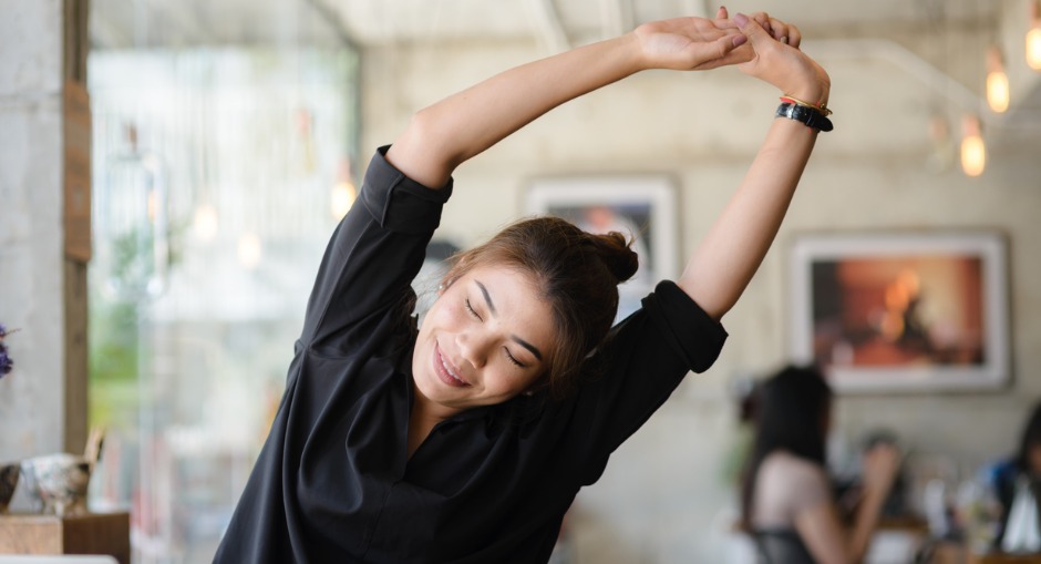 Young female officer worker stretching her lower back while sitting at her desk. 