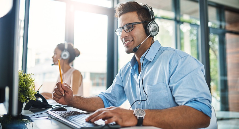 Man using a headset office phone while working with a female colleague in the background.