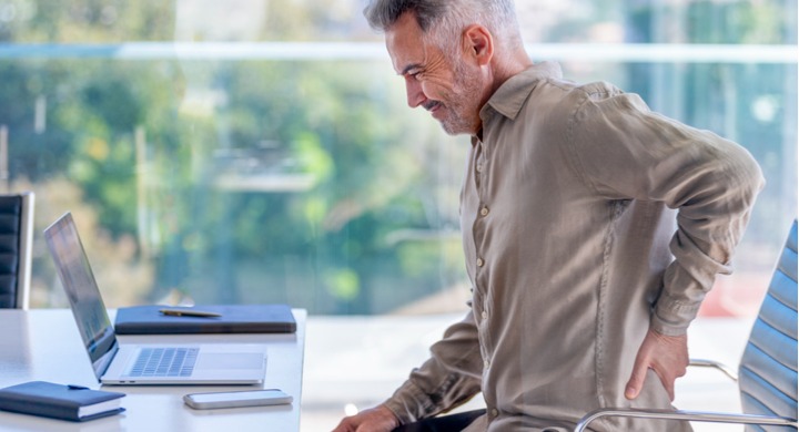 Man struggling with back pain while working at his desk due to poor ergonomics.