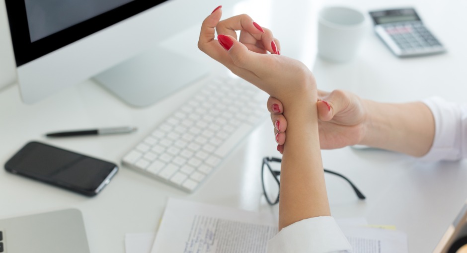 Woman holding her wrist in pain from an RSI while seated at a workstation.