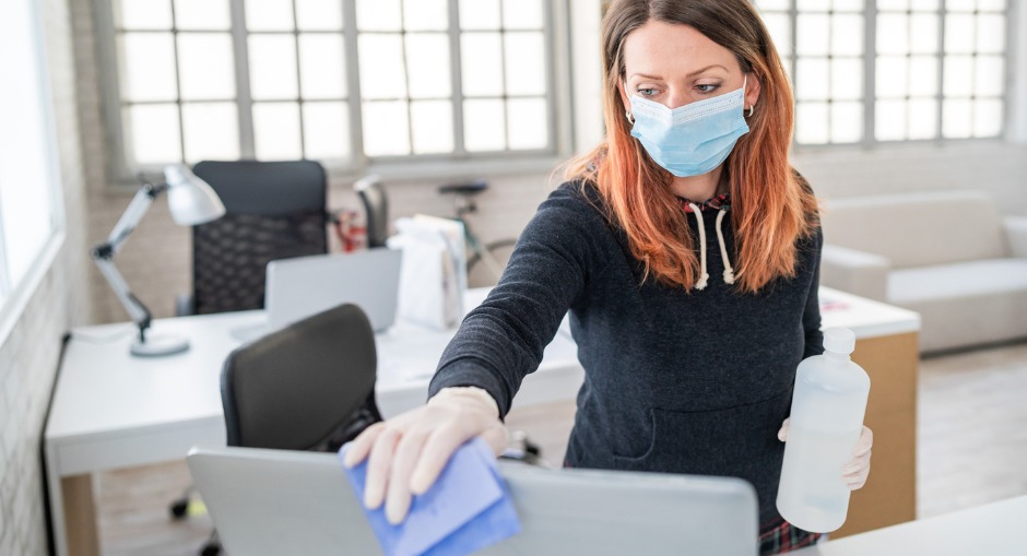 Female office worker disinfecting and sanitising her workstation to protect herself COVID-19