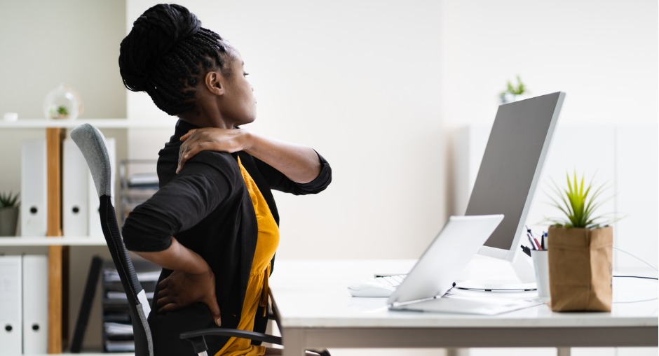 Woman with back pain from a poor ergonomic setup sitting in her office while working.