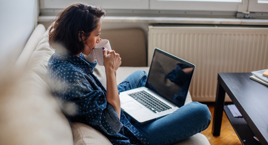 Young woman working from the couch, with a poor ergonomic home office setup