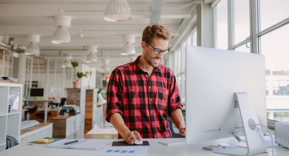 Young male office worker using a height adjustable desk to find how tall his office desk should be