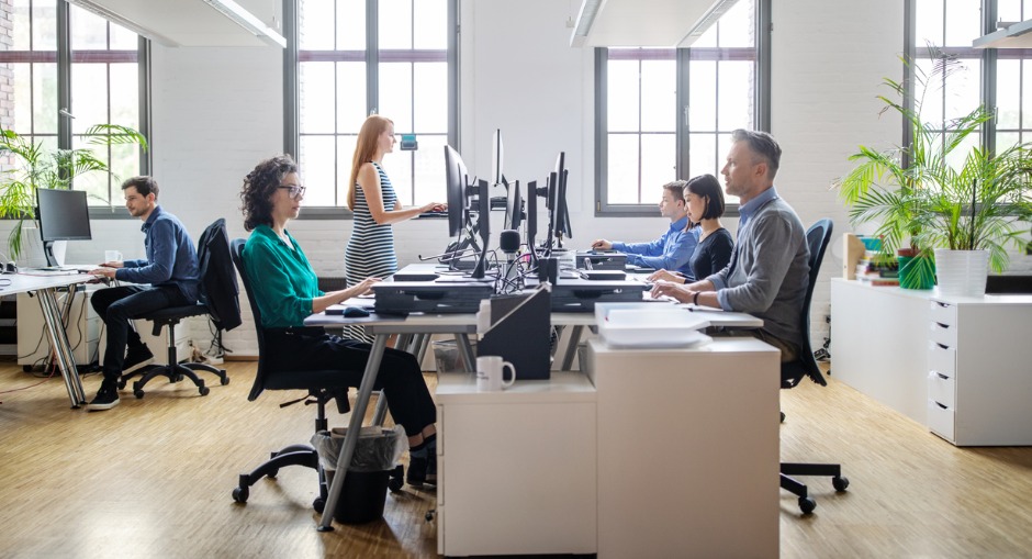 Standing vs sitting at a desk, one worker using an ergonomic sit stand desk